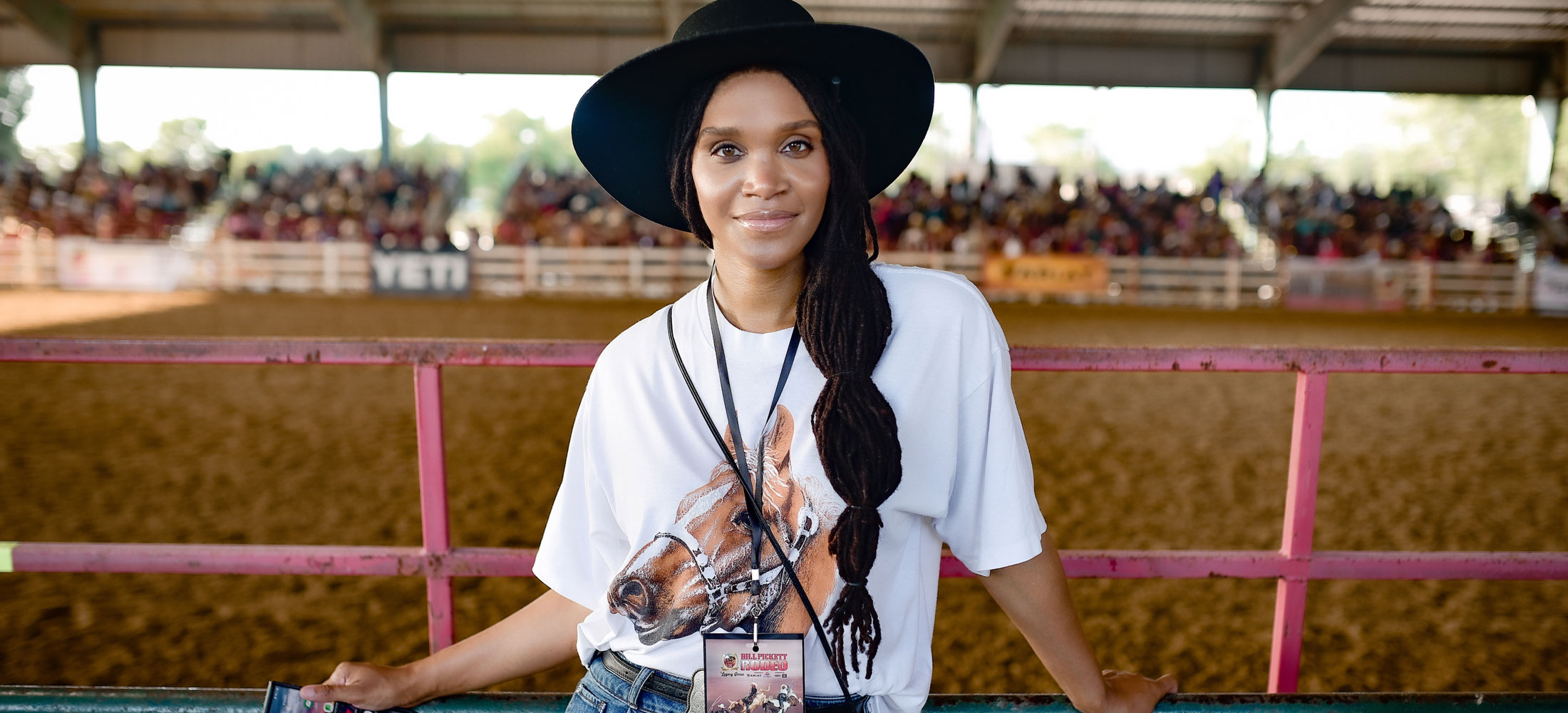 A woman wearing a hat looking directly at the camera, holding a cell phone and posing.